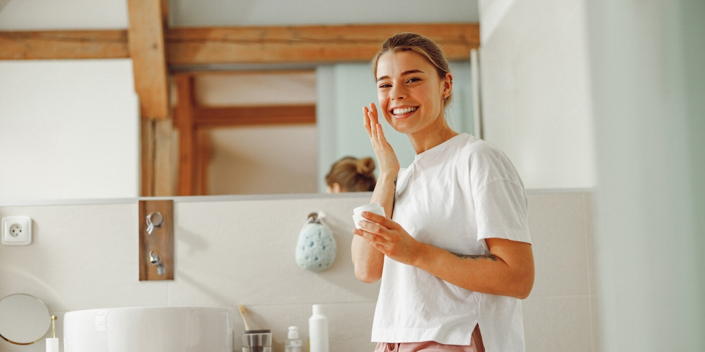 Woman in bathroom looking at camera while doing skincare routine
