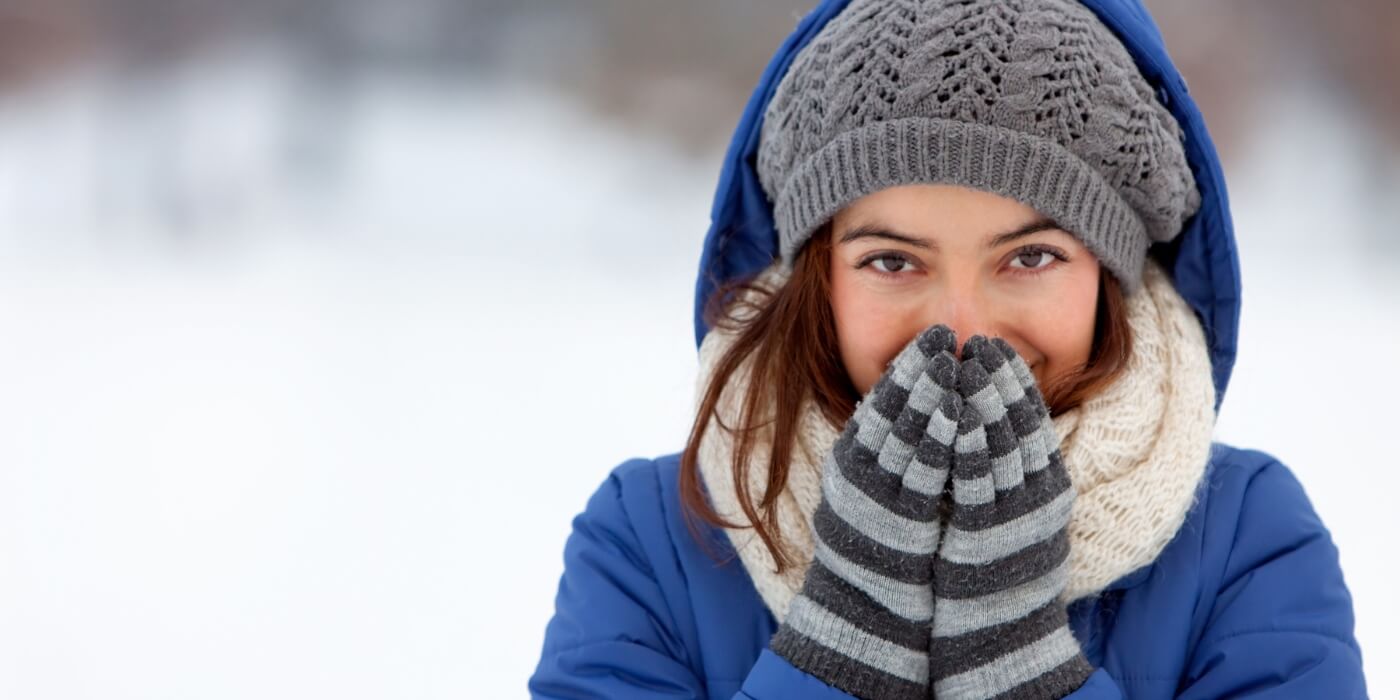 Woman in winter clothes covering her mouth with gloves.