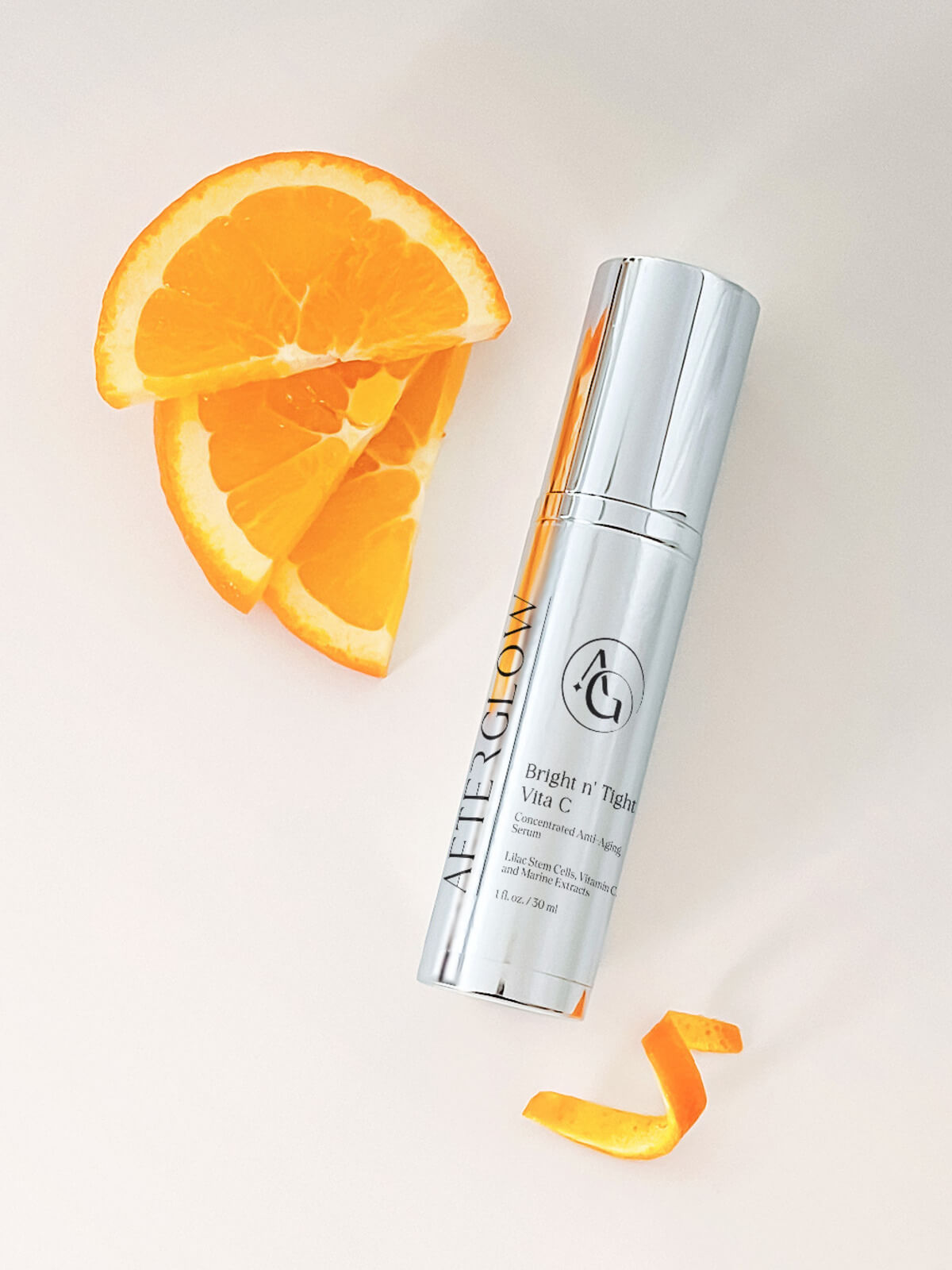 A small shiny container skincare product with the brand name 'afterglow' on it next to 3 orange slices.