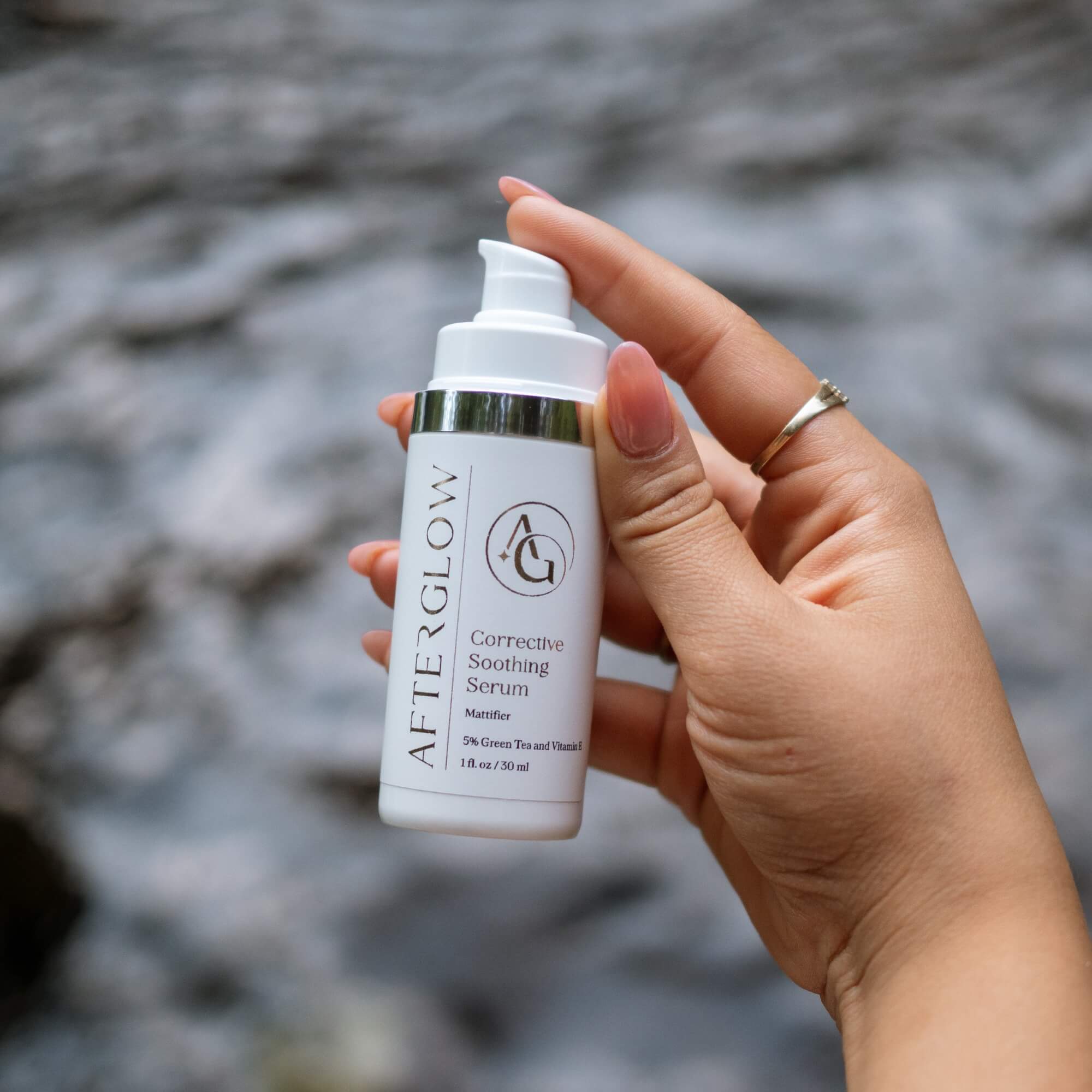 Hand holding a bottle of Afterglow Skin co. corrective soothing serum with a blurred natural background