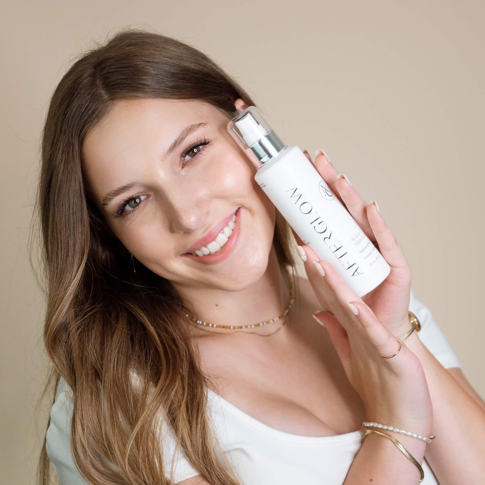 Woman holding Afterglow Skin Co. Hydra C Peptide Spray bottle against a beige background