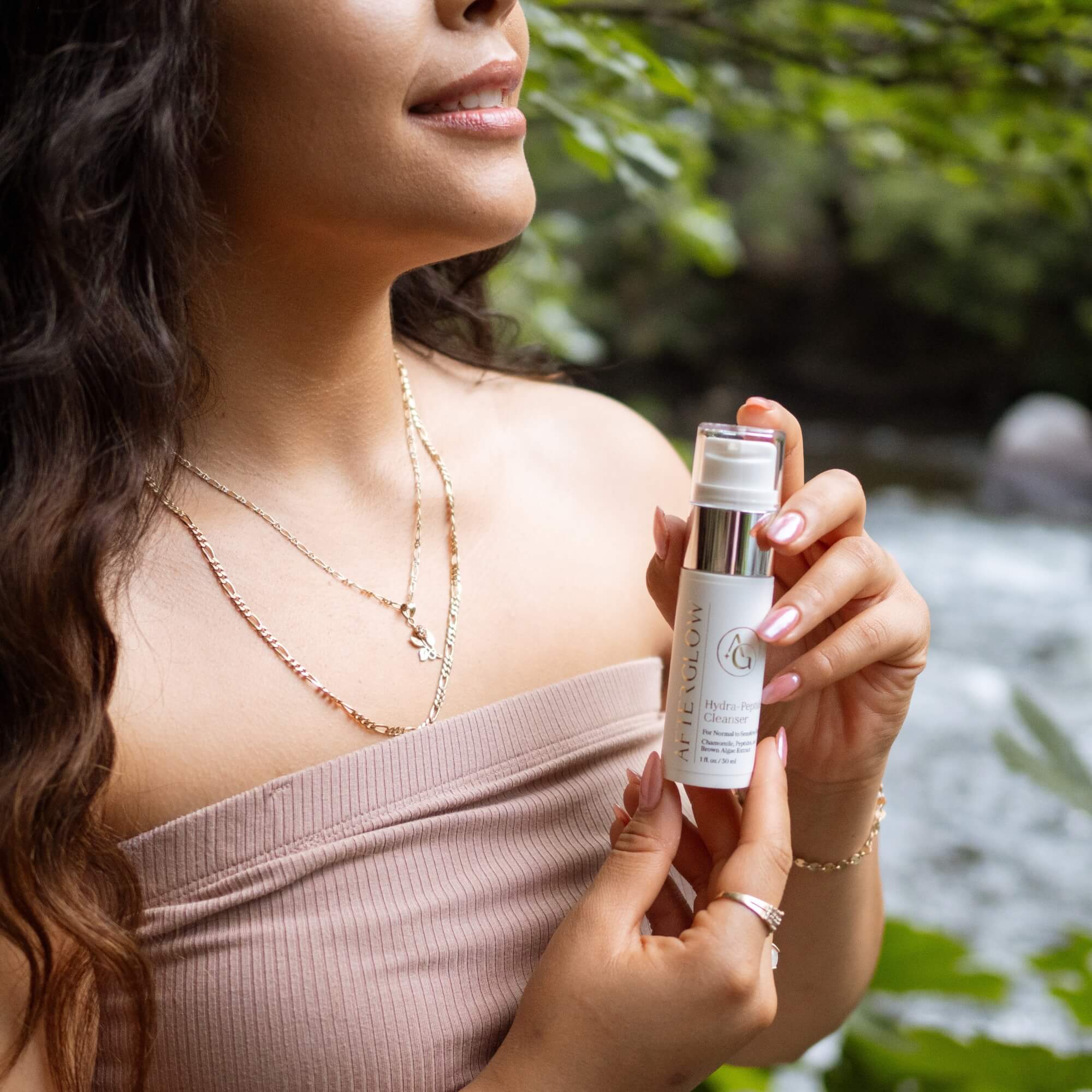 Woman holding a Afterglow Skin Co Hydra Peptide Cleanser with a natural background