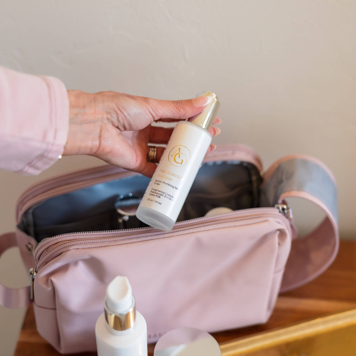 A woman's hand pulling a small spray bottle out of a pink bag.