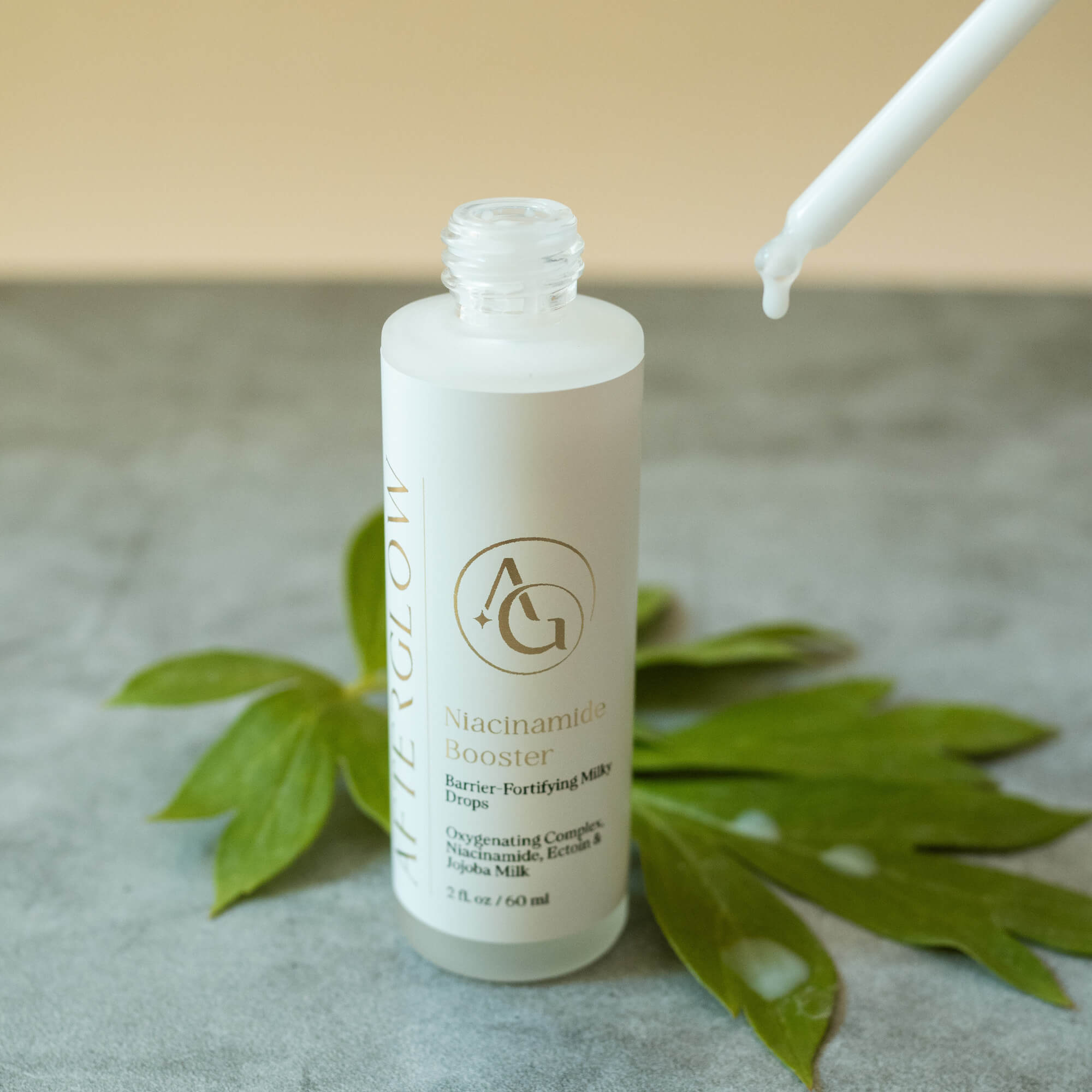 Afterglow Skin Co. Niacinamide Booster with dropper on a textured surface with leaves