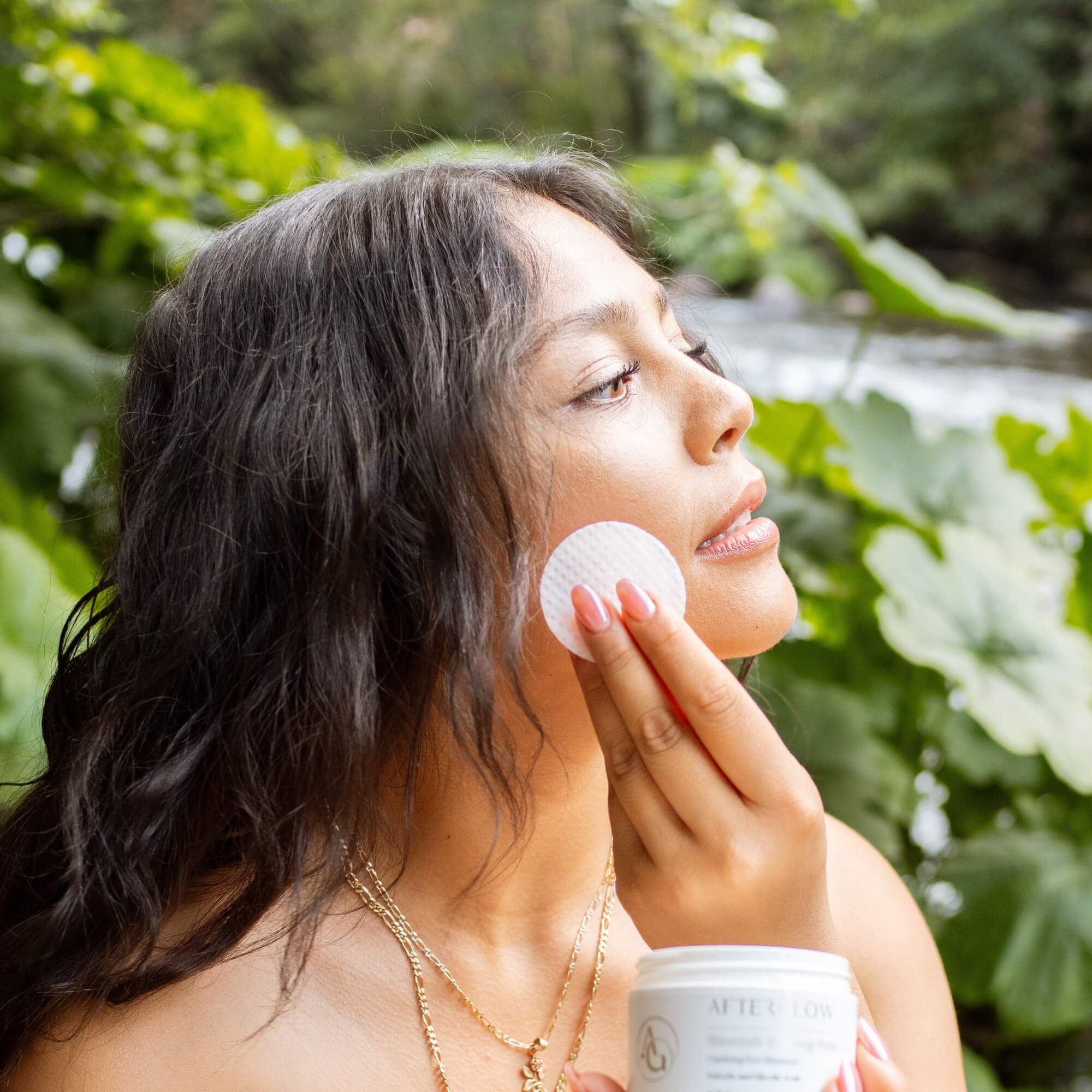 Woman applying Afterglow Skin Co. Skin Perfecting Gel pads to her face outdoors with greenery in the background