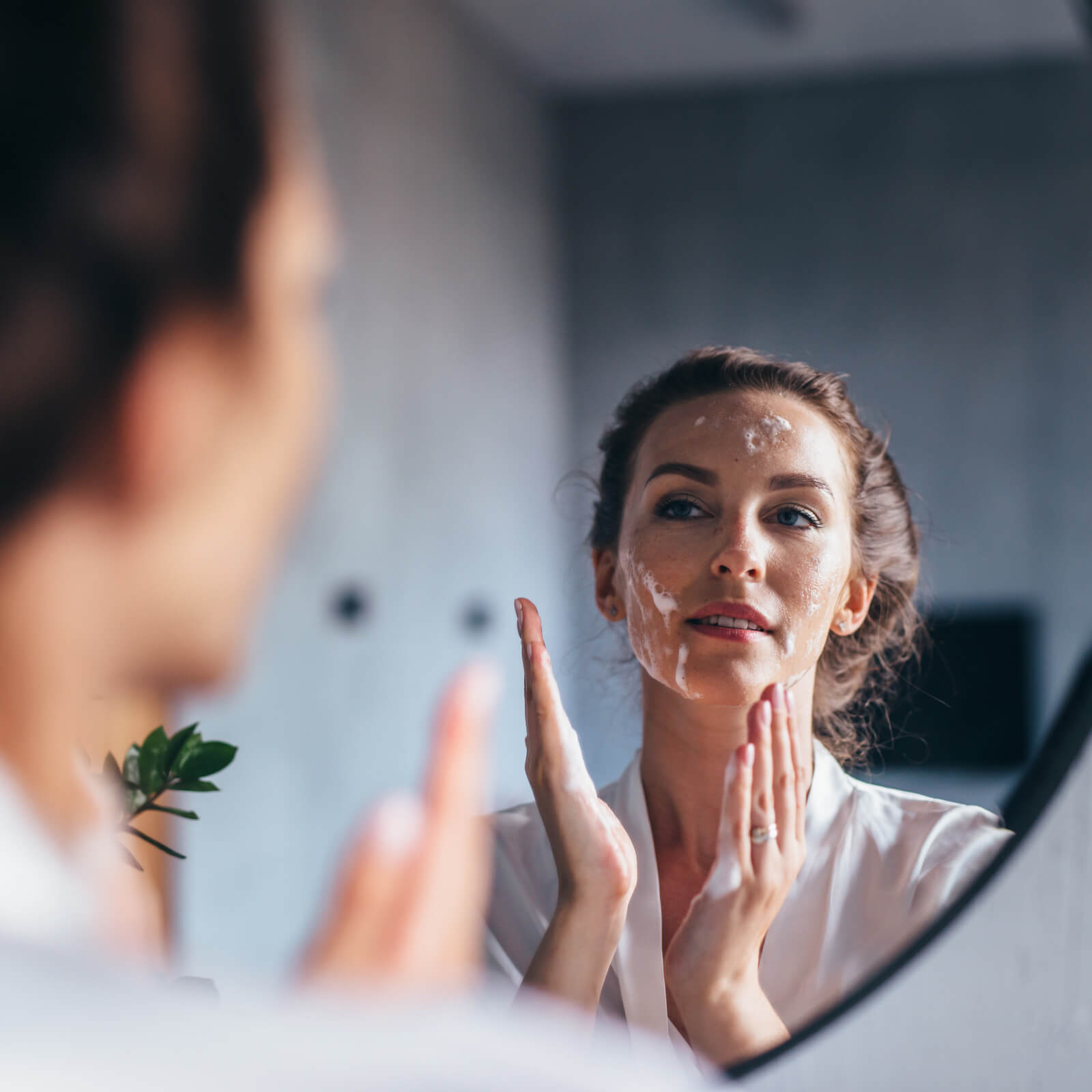 A woman in front of a mirror putting skincare products on her face.