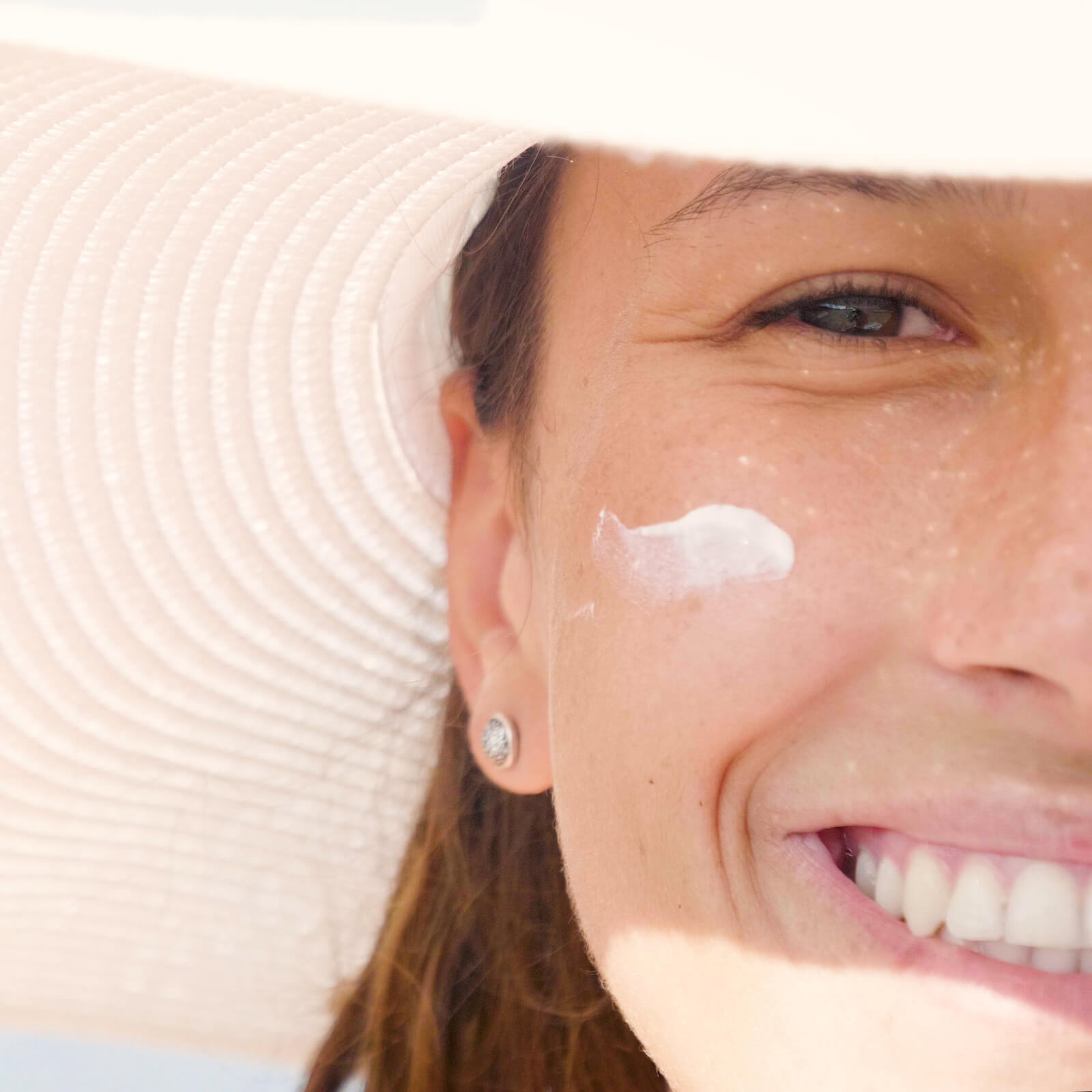 Half of a woman's face smiling with a small swatch of skin care cream under her right eye.