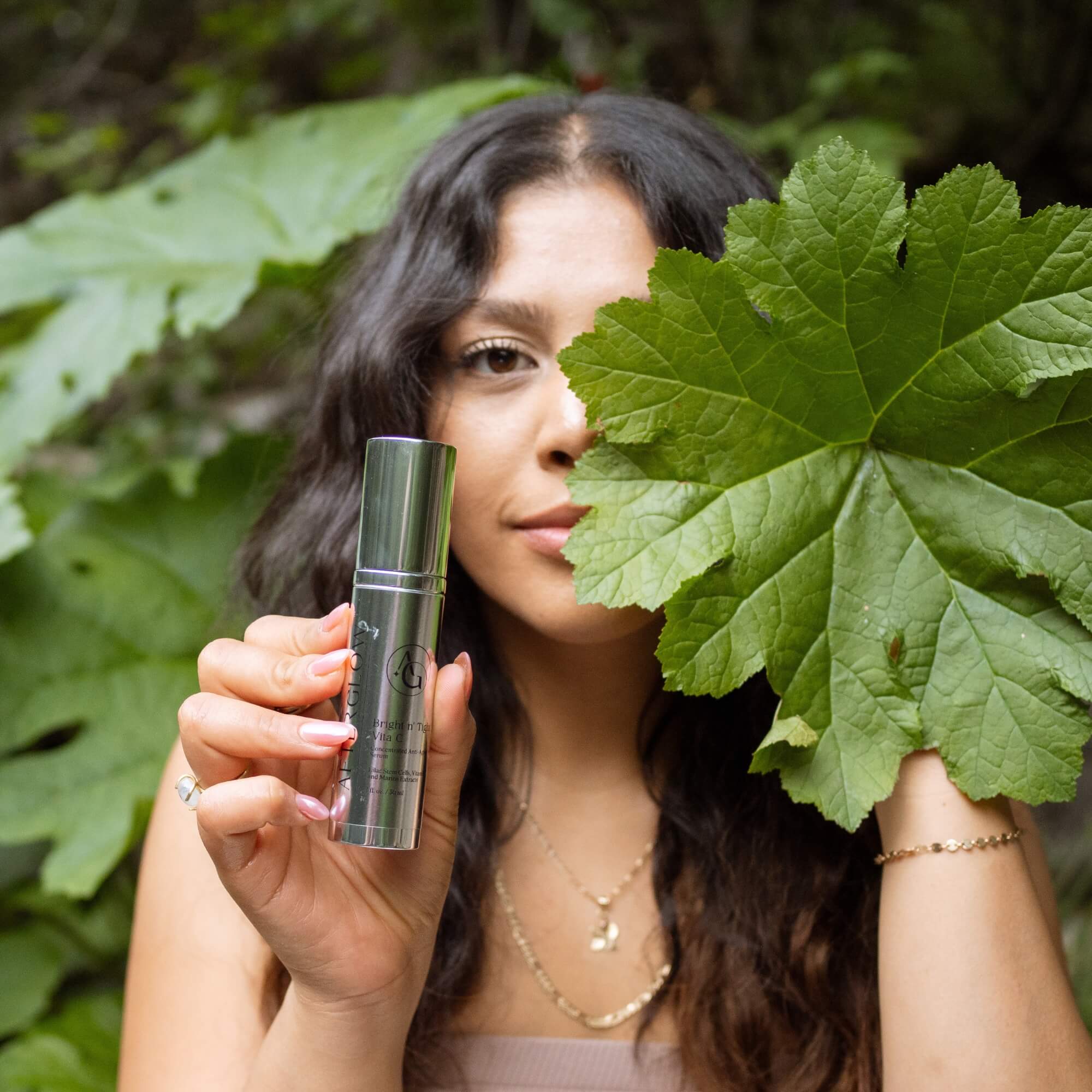 Woman holding a green leafy plant and Afterglow Skin Co Bright n' Tight Vita C bottle against a natural background
