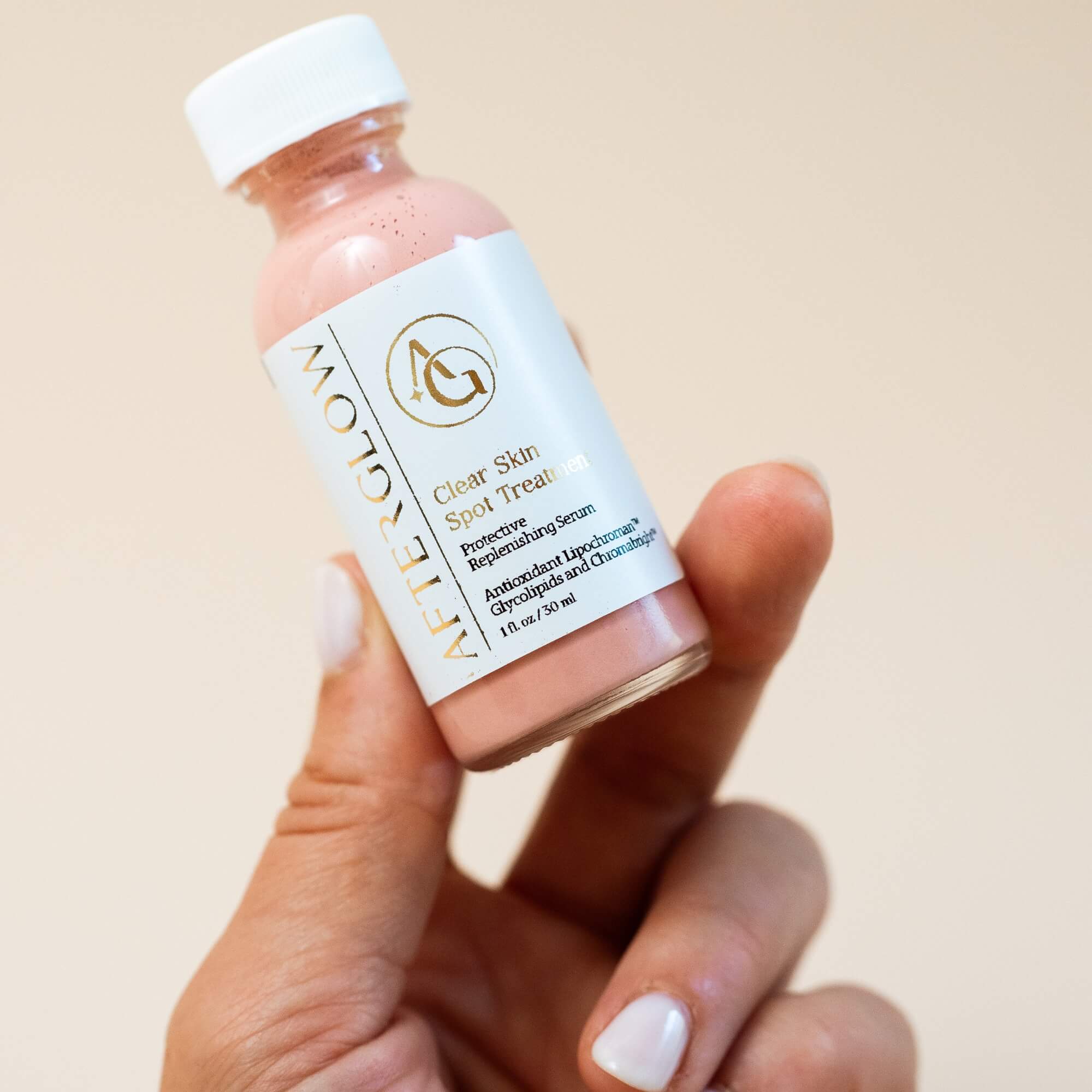Hand holding a bottle of Afterglow Skin Co. Clean Skin Spot Treatment against a beige background