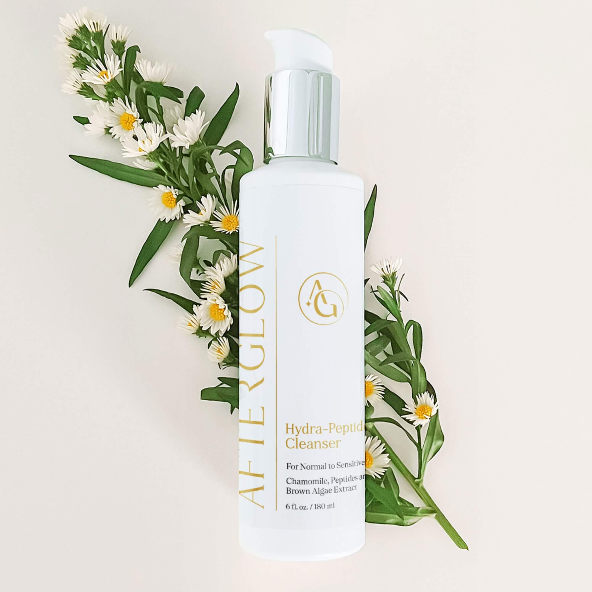 A pump bottle of Afterglow Skin Co. Hydra peptide cleanser in front white flowers with green leaves on a cream background