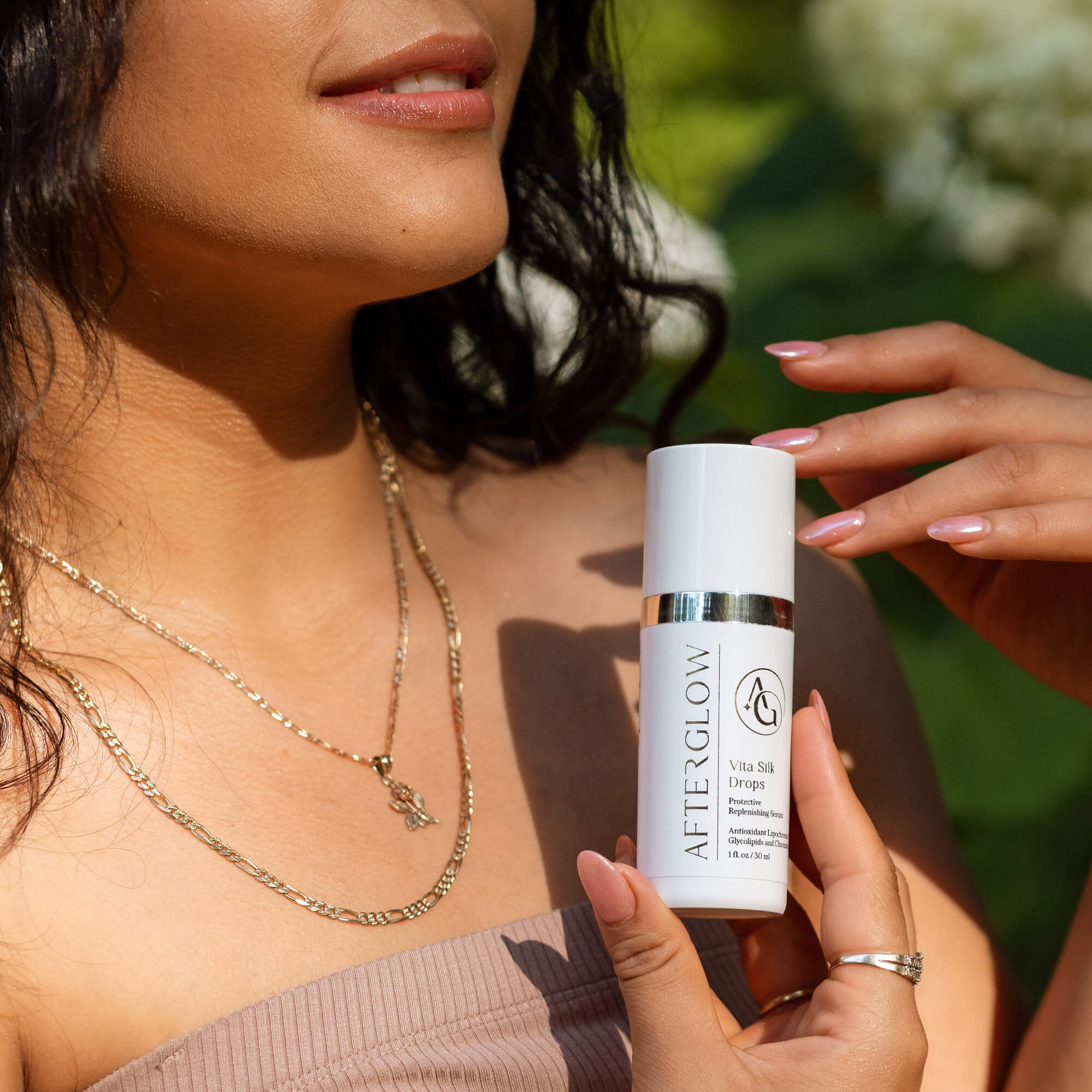 Woman holding Afterglow Skin Co. Vita Silk Drops with a blurred green background